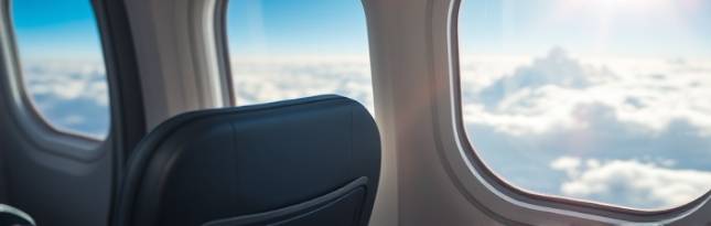 commercial airplane window seat, contemplative, looking out at the clouds, photorealistic, clean windowpane with sun rays filtering through, highly detailed, subtle wing flex, bokeh effect, vibrant sky blue and white, natural sunlight, shot with a 70-200mm lens.